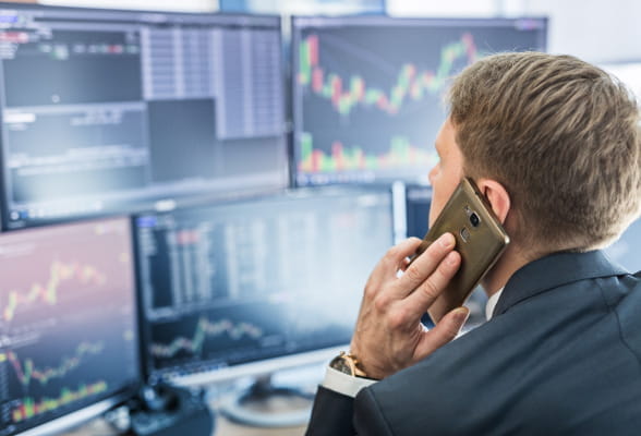 Trader analyzing cotton market price movements on multiple screens while managing risk over a phone call.