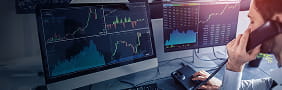 Trader analyzing market charts on multiple screens while on a call, representing StoneX’s sales and trading execution services.